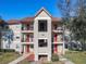 Three story condo building featuring red doors, mature landscaping, and an exterior stairwell under a bright blue sky at 3004 Parkway Blvd # 202, Kissimmee, FL 34747