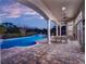 Elegant covered patio with a dining set, ceiling fan, and view of the luxurious swimming pool at dusk at 7471 Gathering Loop, Reunion, FL 34747