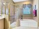 Close-up bathroom view of the glass shower and soaking tub with tan tiling and an elegant curtained window at 328 Hamrick Dr, Kissimmee, FL 34759