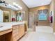 Well-lit bathroom featuring a glass shower, a soaking tub, a window, and double sinks with wooden cabinets at 328 Hamrick Dr, Kissimmee, FL 34759