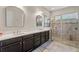 Well-lit bathroom with double sinks, marble countertops, black cabinets, and tiled shower with glass doors at 4774 Rummell Rd, St Cloud, FL 34771