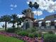 Picturesque Del Webb entrance with a decorative tower, a stone water feature and colorful flower beds at 507 Pamplona Pl, Davenport, FL 33837