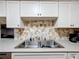 Close-up of the kitchen sink area with white cabinets and stone tile backsplash at 6 Palm Way, Haines City, FL 33844