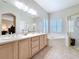 Bright bathroom features double sinks, a soaking tub, a walk-in shower, and plantation shutters at 901 Shorehaven Dr, Poinciana, FL 34759