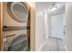 A modern, stacked washer and dryer set sits in a hallway with light gray wood-look floors and a door at 562 Flemming Way # 200, Maitland, FL 32751