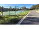 Community tennis court with a dark green fence, surrounded by lush greenery, and an adjacent sidewalk at 10210 Hartford Maroon Rd, Orlando, FL 32827