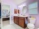 Bathroom featuring double sinks, wood cabinets, lilac walls, and an open doorway at 649 Meadow Pointe Dr, Haines City, FL 33844