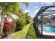 A view of a screened-in pool, green lawn and red tropical plants, and palm trees at 16694 Olive Hill Dr, Winter Garden, FL 34787