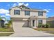 Two-story home featuring neutral colors, dark shutters, attached garage, and green landscaping under a blue, partly cloudy sky at 293 Pineywoods St, St Cloud, FL 34772