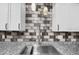 Close-up of a modern kitchen sink with granite counters, tiled backsplash, and white cabinets at 4172 Stonehenge Rd, Mulberry, FL 33860