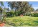 A lush green backyard featuring a red bench and mature trees, offering a serene outdoor space at 401 Woodlawn Ter, Kissimmee, FL 34744