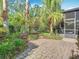 Paver patio leading to a well-landscaped backyard with tropical plants, a metal fence, and a screened enclosure at 133 Indian Wells Ave, Kissimmee, FL 34759