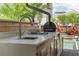 Outdoor kitchen with grill, sink, and counter, overlooking a pool and tropical foliage at 13041 Gabor Ave, Orlando, FL 32827