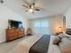 Well-lit bedroom featuring a ceiling fan, wood dresser with TV, and a cozy chair by the window at 129 Pine Lake View Dr, Davenport, FL 33837