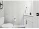 A half bath with a toilet and single sink vanity with white cabinets, black handles and fixtures and light gray paint at 16035 Wilkinson Dr, Clermont, FL 34714