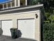 Two-car garage exterior showcasing white doors, beige siding, and the neighborhood trash receptacle at 910 Spring Park St # 103, Celebration, FL 34747