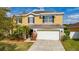 Inviting two-story home featuring a two-car garage, lush landscaping, and a sunny yellow facade at 10937 Prairie Hawk Dr, Orlando, FL 32837