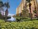 Scenic view of a tall building surrounded by palm trees, lush greenery, and a tranquil canal at 8125 Resort Village Dr # 5310, Orlando, FL 32821