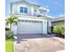 Two-story home featuring a white garage door, brick driveway and trimmed palm trees in a landscaped yard at 6608 Harper Way, Harmony, FL 34773