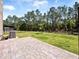 Landscaped backyard with brick paver patio, AC unit, black fence and a tree line at 3038 Camden Way, Davenport, FL 33837