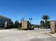 Gated community entrance with stone pillars, a black iron gate, and manicured landscaping under a blue sky at 939 Anna Pl, Davenport, FL 33837