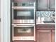 Close-up of stainless steel double ovens with granite countertops and mosaic tile backsplash at 363 Bella Cortina Dr, Kissimmee, FL 34759