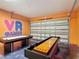 This game room has a shuffleboard table and an air hockey table set against vibrant orange walls with 