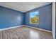 A blue bedroom featuring a window view of trees, wood-look flooring, and a closet at 638 Kangaroo Dr, Poinciana, FL 34759