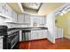 Cozy kitchen featuring black appliances, wood floors, white cabinetry, and laundry access at 2430 Mill Run Blvd, Kissimmee, FL 34744