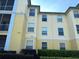 Close-up of exterior apartment building with large windows, hedges, and yellow siding at 8809 Dunes Ct # 201, Kissimmee, FL 34747