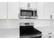 Close-up of stainless steel microwave and range featuring white cabinets, quartz countertops, and tile backsplash at 1067 Cloud Ridge Ct, Mount Dora, FL 32757