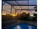 A beautiful screened-in pool shimmers beneath a vibrant, colorful sunset at 1920 Triumfo Cir, Kissimmee, FL 34744