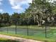 Community tennis court surrounded by mature trees and a black chain link fence at 2901 Puerta Del Sol Blvd, Kissimmee, FL 34744