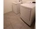 Laundry area with white front-load washer and dryer set against neutral tile flooring at 11273 Amber Ridge Dr, Zellwood, FL 32798