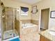 Bright bathroom featuring a glass-enclosed shower, soaking tub, neutral tile, and granite countertop at 2888 Spring Breeze Way, Kissimmee, FL 34744