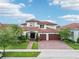 Elegant Mediterranean-style home with a tile roof, lush landscaping, brick driveway, and attached three-car garage at 13136 Alderley Drive Dr, Orlando, FL 32832
