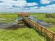 Scenic view of a long wooden dock leading to a covered boathouse, surrounded by a serene lake filled with lily pads at 1654 Marina Lake Dr, Kissimmee, FL 34744