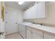 Bright laundry room with white cabinets, tile counters, laundry sink, washer and dryer at 1258 Donalds Pl, The Villages, FL 32162
