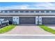 View of townhome garages featuring brick paver driveway, green grass and landscaping, and black carriage door hardware at 12190 Plumpton Dr, Winter Garden, FL 34787