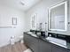 Bathroom with double sink, black countertop, sleek gray cabinets, and illuminated mirrors at 1425 Serendipity Ln, Clermont, FL 34714