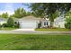 Charming single-story home with a two-car garage, lush green lawn, and manicured landscaping at 7013 Beargrass Rd, Harmony, FL 34773