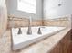 Close up of the large white soaker tub with stone tile and decorative tile border at 1470 Lake Side Ave, Davenport, FL 33837