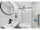 Modern bathroom featuring a round mirror, white sink, toilet, and stylish white tiled shower with black hardware at 1626 Gar St, St Cloud, FL 34771