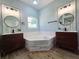 Bright bathroom featuring a tub, a window, dual sinks, mirrors, and wood-look vinyl flooring at 2312 Twickingham Ct, Clermont, FL 34711