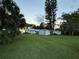 View of backyard with lush lawn, mature trees, and sheds; partial lake view in distance at 2740 Barker Rd, St Cloud, FL 34771