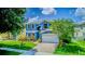 Inviting two-story blue home boasts vibrant landscaping and a paver driveway leading to a garage at 12715 Moss Park Ridge Dr, Orlando, FL 32832