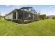 Landscaped backyard with healthy green lawn and screened in patio, edged with decorative shrubs at 1703 Encinitas Way, Kissimmee, FL 34759