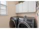 Practical laundry room with modern gray front load washer and dryer, upper cabinets, and a bright window at 15037 Cedar Branch Way, Orlando, FL 32824