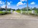 Scenic gated driveway leads to a home with lush greenery and mature trees under a bright blue sky and fluffy clouds at 5150 Gentry Oaks Pl, St Cloud, FL 34772