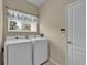 Bright laundry room featuring a side-by-side white washer and dryer, window with blinds, and adjacent access door at 4065 Kingsley St, Clermont, FL 34711